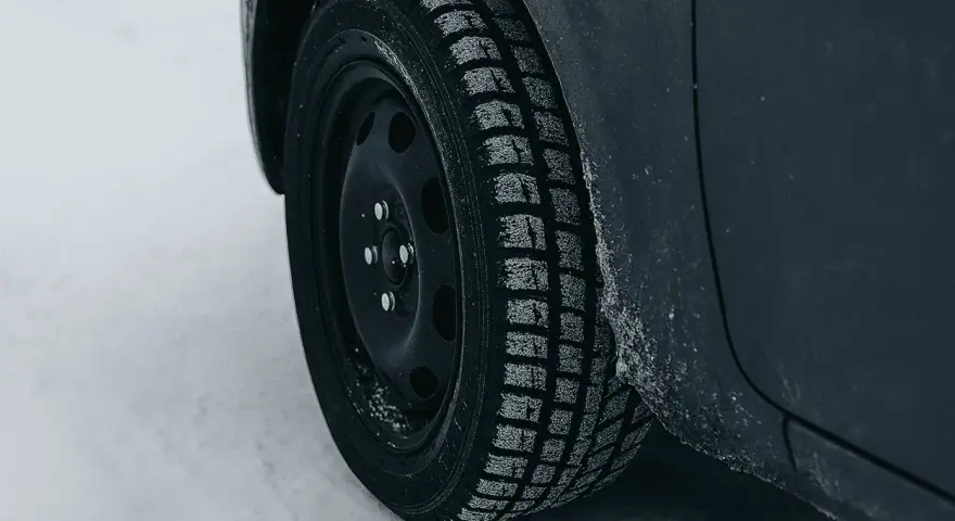 Ruota di un'auto con pneumatico invernale coperto di brina, pronto per affrontare la neve. La scheda pneumatici è fondamentale per la sicurezza.