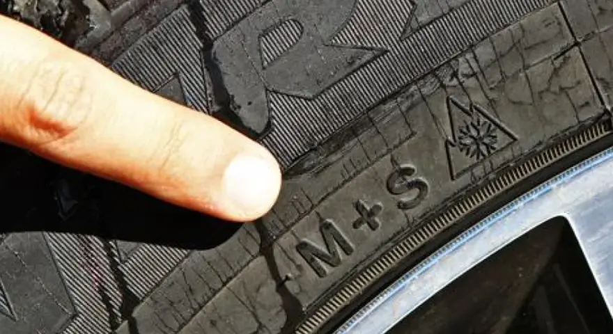 Dito indice indica il simbolo del fiocco di neve su un battistrada gomme invernali M+S, pronto per la neve.