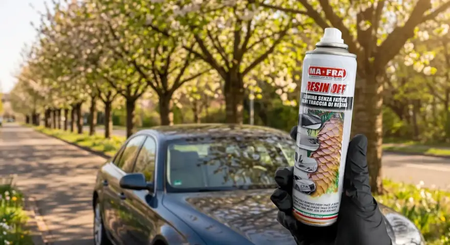 Mano guantata tiene spray MAFRA Resin Off per rimuovere resina e lucidare la plastica dell'auto, con auto scura sullo sfondo.