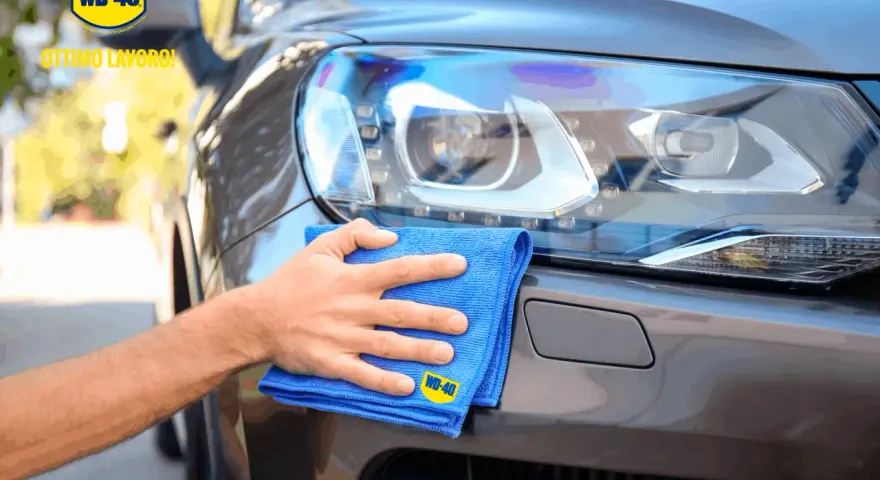 Mano che lucida fari auto con WD-40 e panno blu. Ottimo lavoro!
