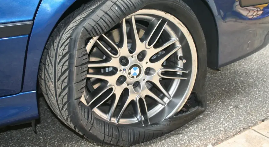 Un pneumatico squarciato sul cerchione di un'auto blu. La gomma è completamente sgonfia e deformata, mostrando il danno.