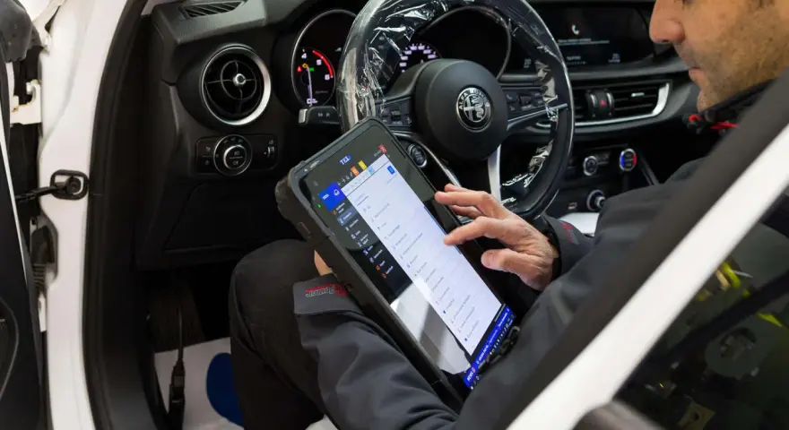 Meccanico usa tablet per diagnosticare la centralina auto. Il dispositivo mostra le opzioni di controllo e i dati del veicolo.