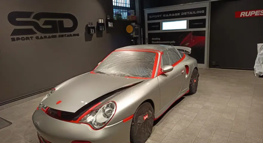 Auto sportiva pronta per la verniciatura, con protezioni rosse e cellophane. Il logo "SGD Sport Garage Detailing" è visibile.