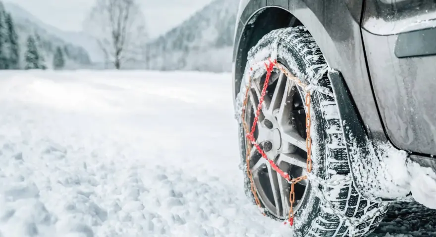 Ruota di un'auto con catene da neve su una strada innevata. Per affrontare la neve, quante catene da neve servono? Di solito due, una per ogni ruota motrice.