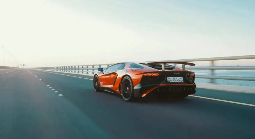 Arancia Lamborghini sfreccia su un ponte, i suoi cavalli scatenati sull'asfalto. L'auto sportiva domina la scena, un'icona di velocità.