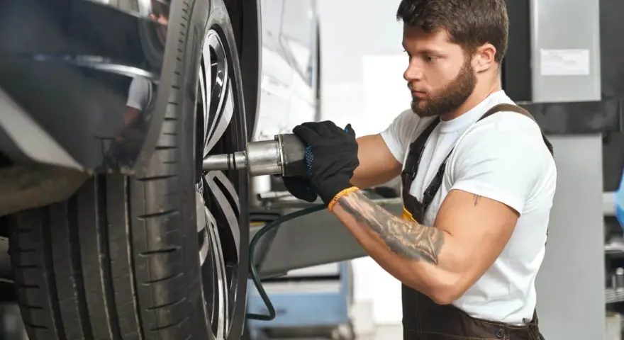 Meccanico con guanti neri lavora su una ruota. Per sapere ogni quanto girare le gomme, consulta il manuale dell'auto.