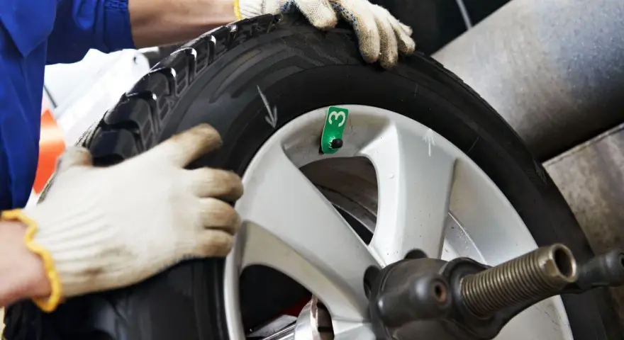 Tecnico con guanti esegue equilibratura gomme per eliminare vibrazioni. Ruota su macchinario specifico.