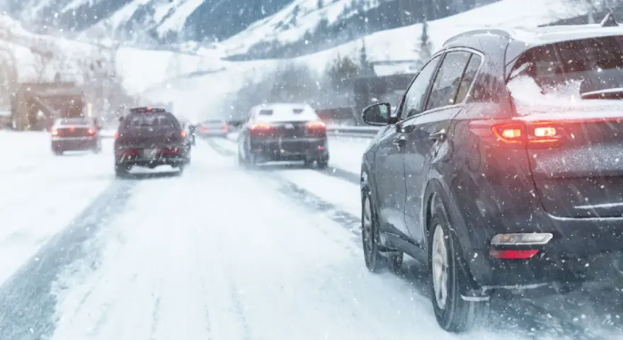 Auto con trazione posteriore sulla neve, luci accese, in un paesaggio montano innevato.