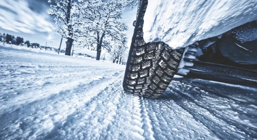 La gomma ghiaccio affronta la neve su una strada invernale, lasciando profonde tracce. Alberi innevati sullo sfondo.