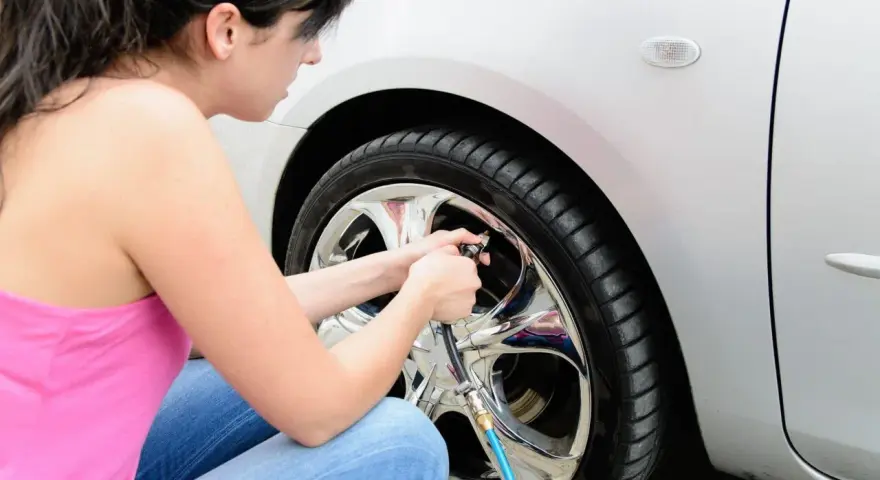 Donna in jeans e canotta rosa usa un compressore per gonfiare le gomme dell'auto, assicurandosi che siano alla pressione giusta.