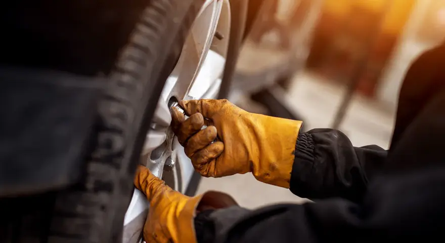 Mani guantate stringono bulloni ruota auto, seguendo la tabella coppia serraggio per sicurezza.