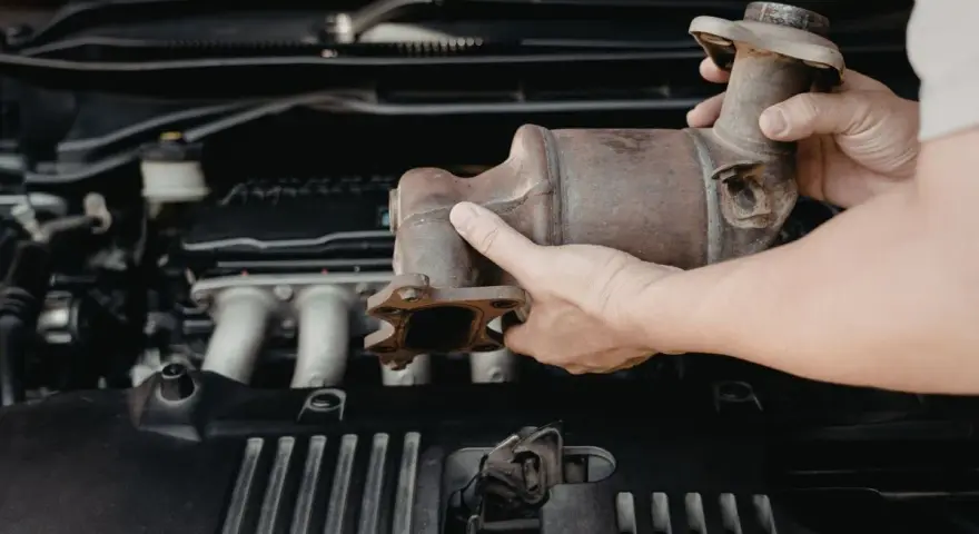 Mani che rimuovono un catalizzatore arrugginito dal vano motore di un'auto. Riparazione del fap auto.