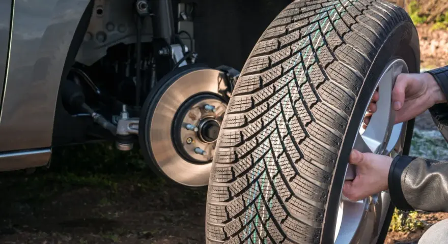 Mani che montano una gomma nuova su un cerchio, con il mozzo dell'auto visibile. La rotazione gomme auto è fondamentale per l'usura uniforme.