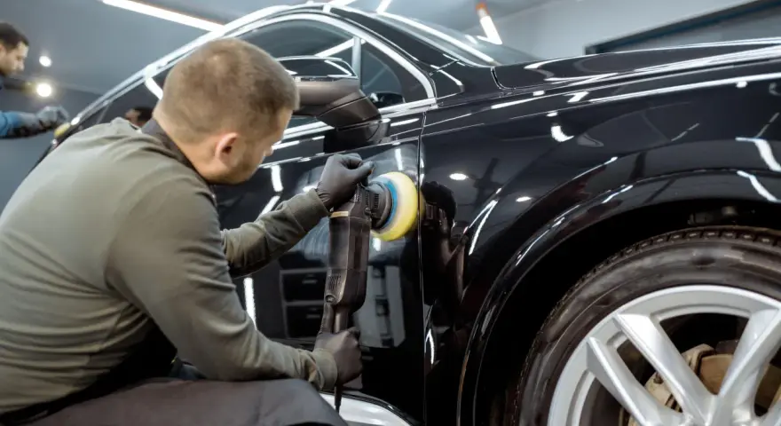 Dettaglio di un professionista che lucida una carrozzeria metallizzata nera per eliminare graffi, con lucidatrice rotativa.