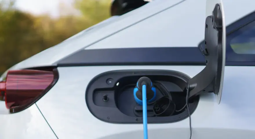 Auto elettrica in carica, con cavo blu collegato alla porta. La coppia motore è pronta per la prossima avventura.