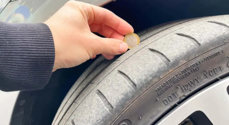 Una mano tiene una moneta da 1 euro per mostrare quanti mm di battistrada ha un pneumatico nuovo. Il battistrada è usurato.