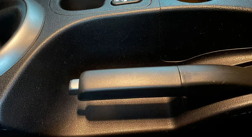 Maniglia del freno di servizio in un'auto, con portabicchieri e pulsante di blocco nelle vicinanze.