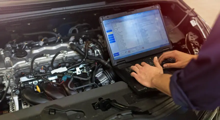 Meccanico controlla il motore di un'auto con un laptop, analizzando dati per ottimizzare l'anticipo automatico motori diesel.