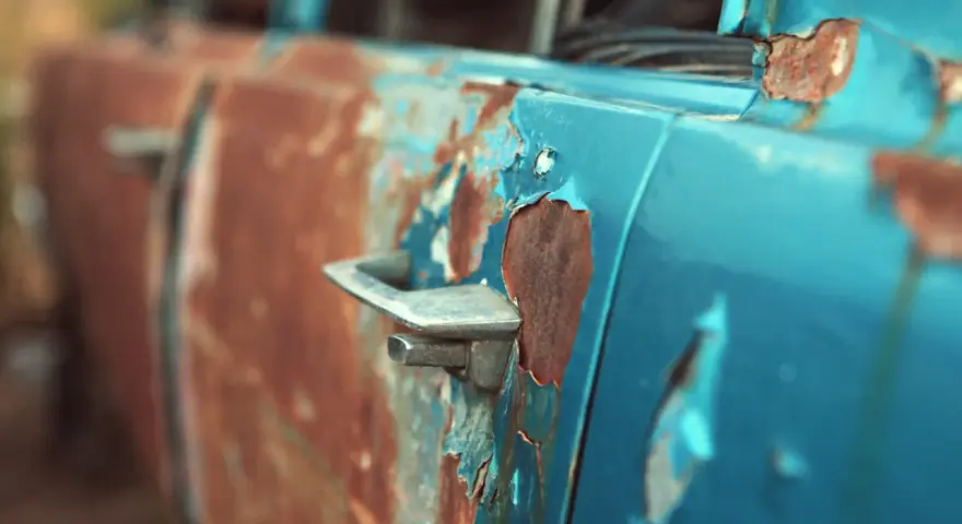 Portiera di un'auto blu con vernice scrostata e ruggine evidente. Un lavoro di restauro per togliere la ruggine sarebbe necessario per riportarla al suo antico splendore.