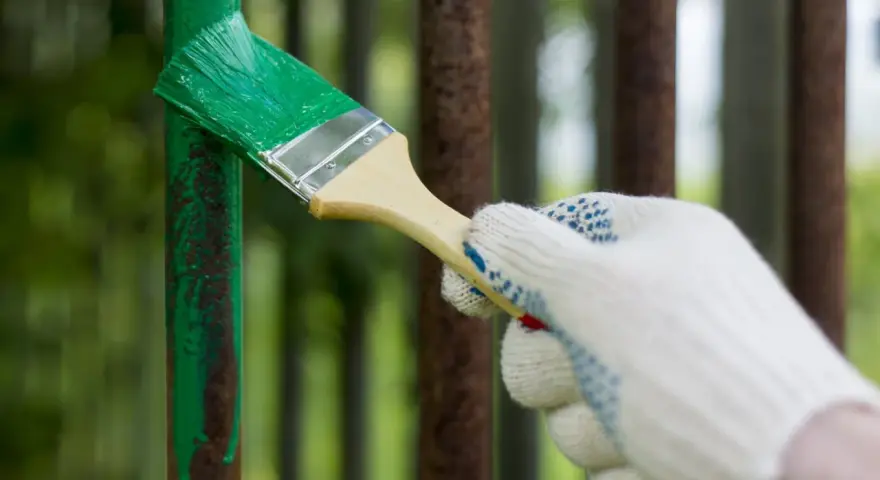 Mano guantata che inizia a verniciare ferro arrugginito con vernice verde brillante, dando nuova vita a una vecchia ringhiera.