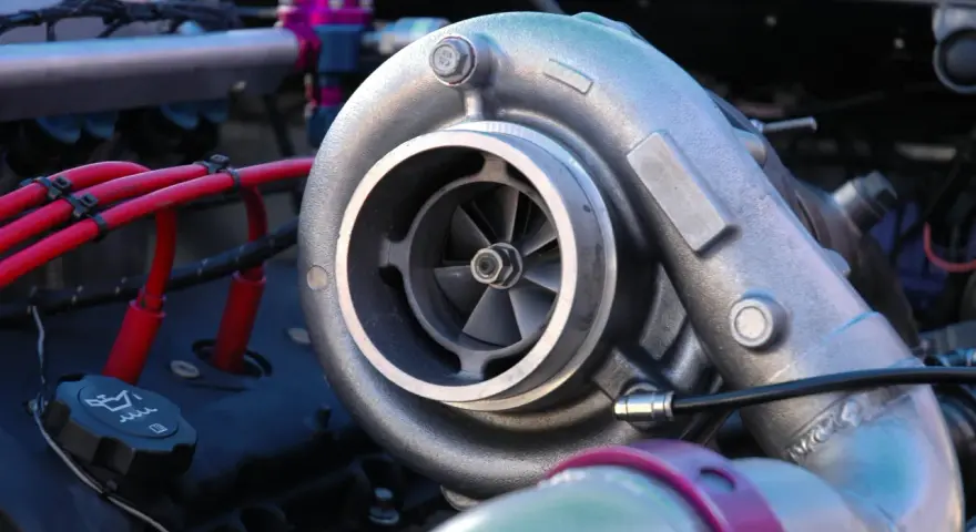 Dettaglio di un motore con un turbo benzina cromato, cavi rossi e un tappo dell'olio.