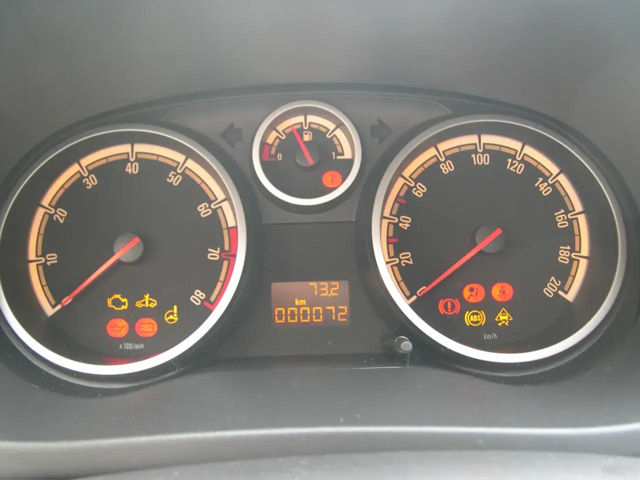 Cruscotto di una Opel Corsa con spie accese: motore, ABS, controllo stabilità. Chilometraggio 72 km.