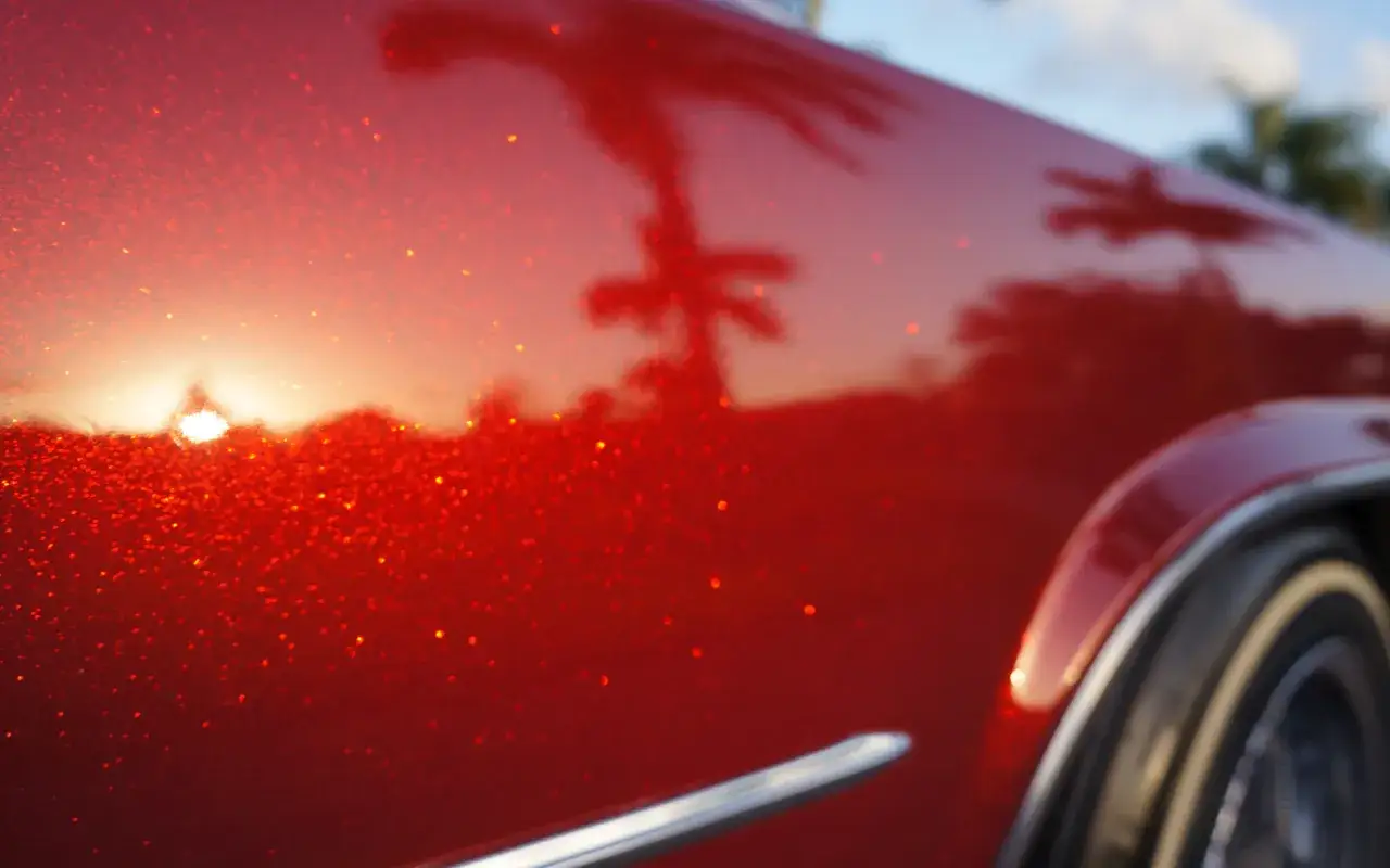 La lucida vernice rosso candy apple riflette palme e tramonto su un'auto d'epoca.