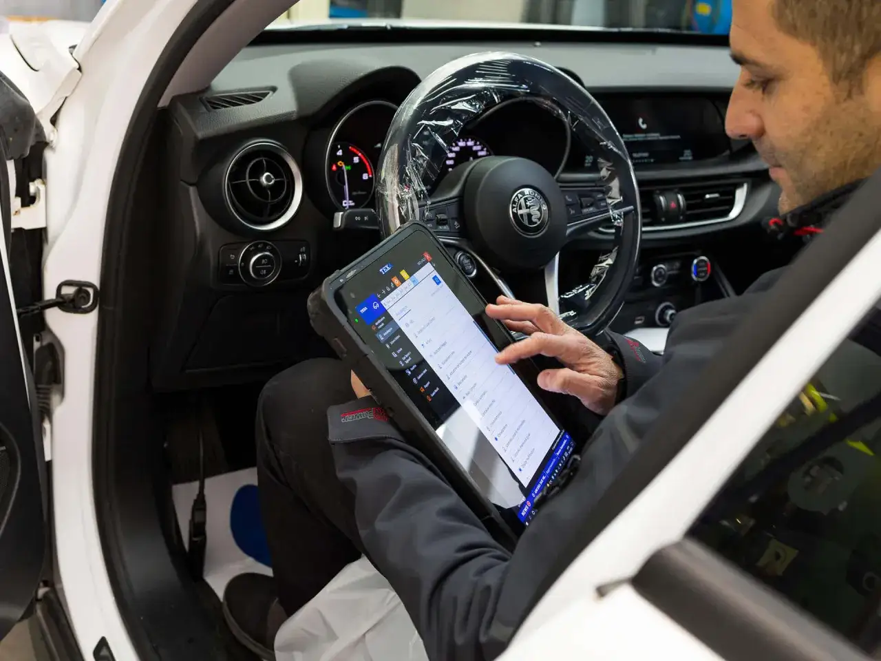 Meccanico controlla il tablet per il sostituzione centralina auto costo. Diagnostica elettronica su Alfa Romeo.