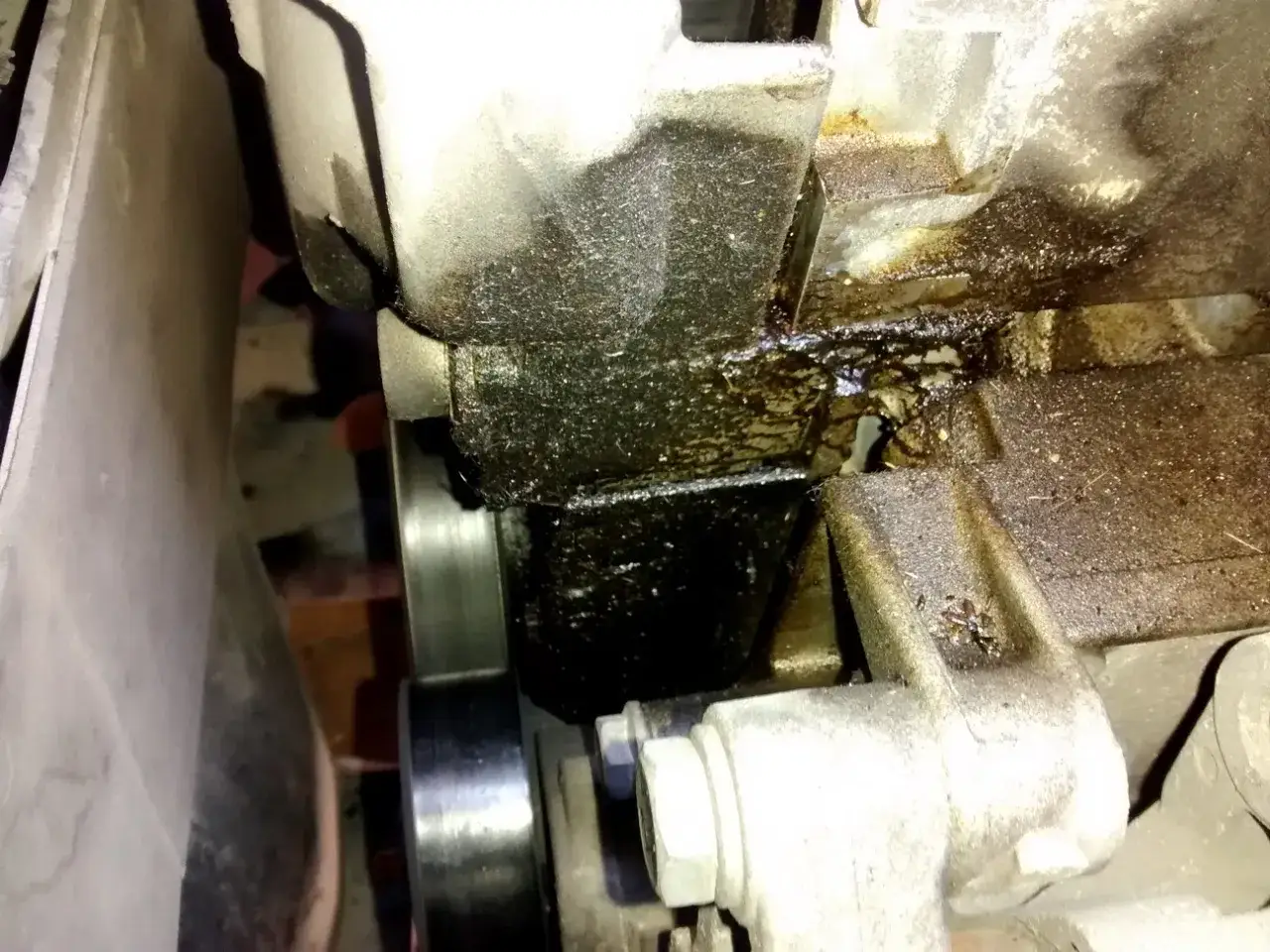 Evidente perdita olio motore dalla testata, con accumuli scuri e vischiosi che colano su componenti meccanici.