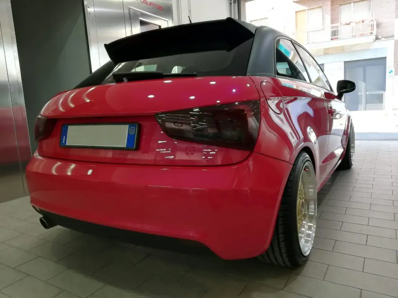 Audi rossa con vernice perlata o metallizzata che brilla sotto le luci. Cerchi dorati e neri, spoiler posteriore.