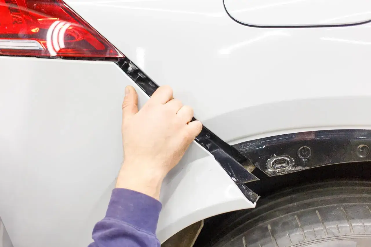 Mano che lavora alla riparazione paraurti in plastica di un'auto bianca.