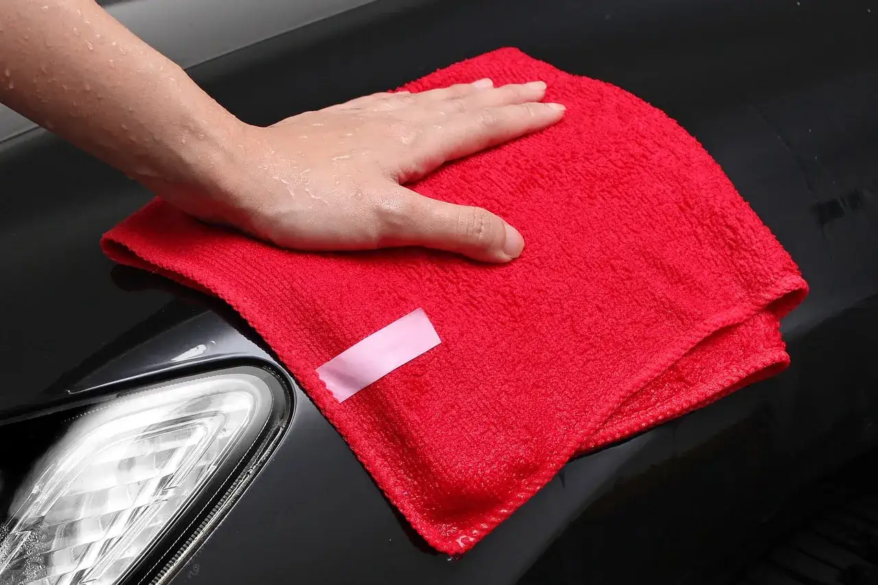 Mano umida che pulisce la carrozzeria dell'auto con un panno rosso per togliere resina.