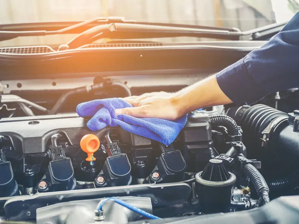 Mano pulisce motore auto con panno blu. Valutare pro e contro lavaggio interno motore per mantenerlo efficiente.
