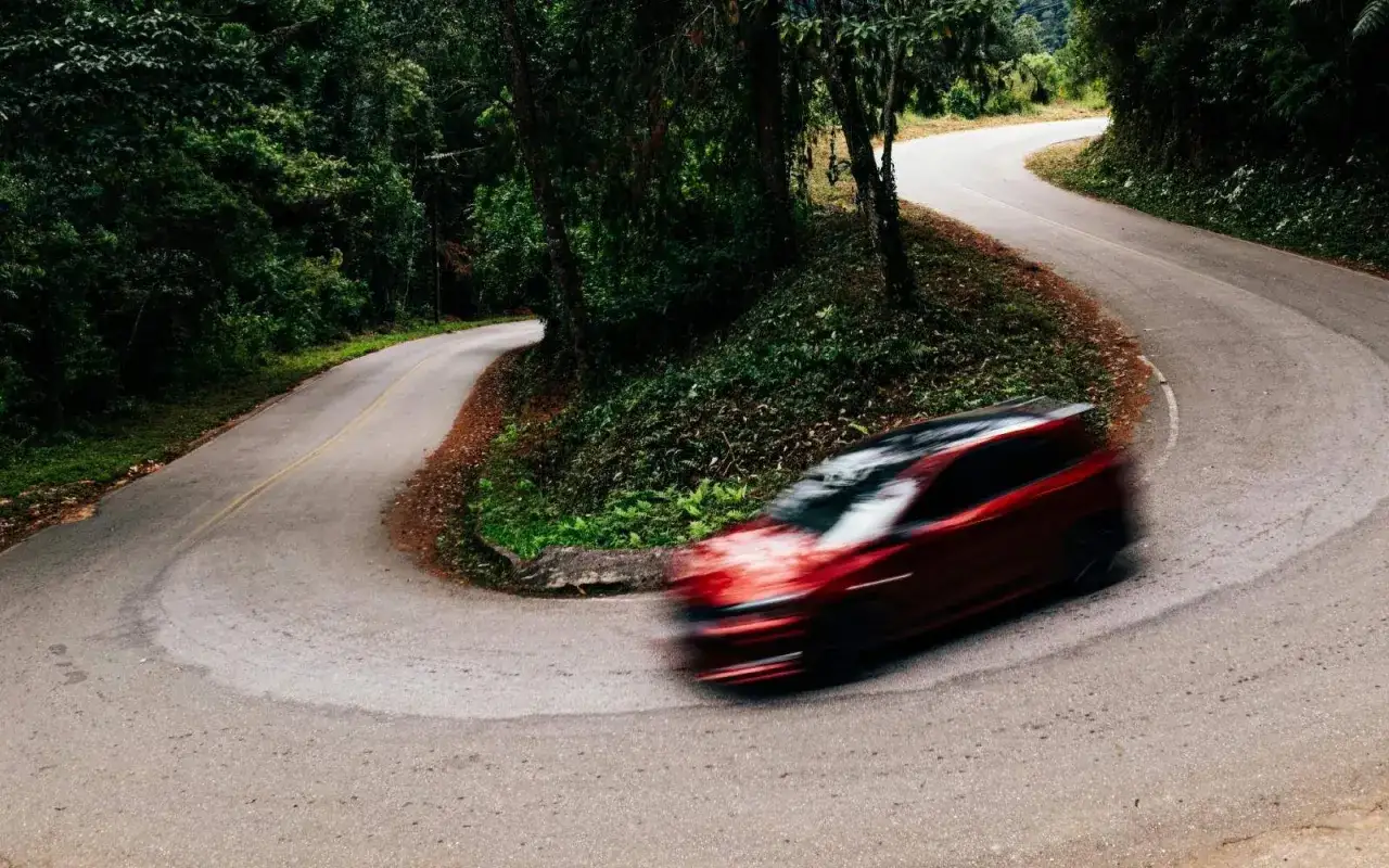 Auto rossa in curva su strada tortuosa tra alberi. Il freno motore aiuta a controllare la velocit&agrave; in discesa.