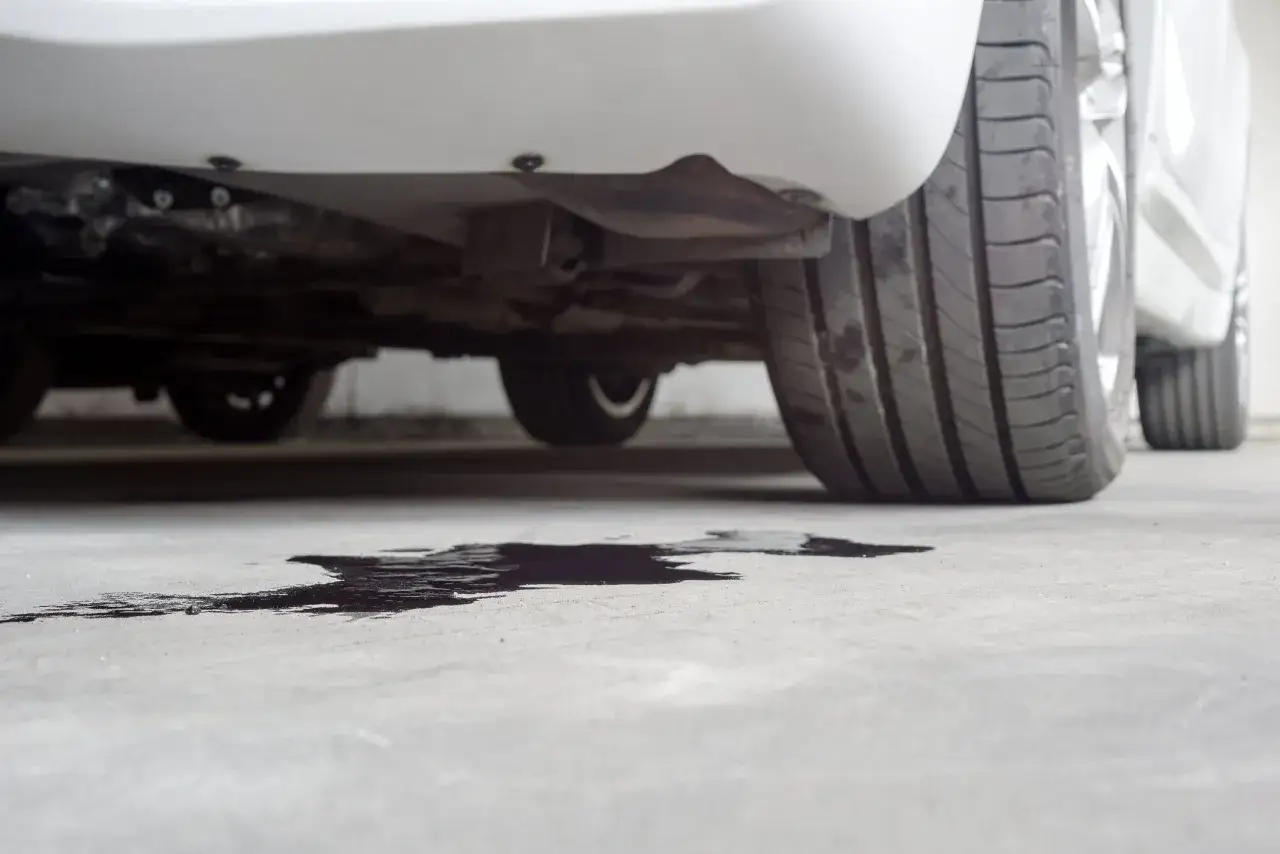 Macchia scura sul cemento sotto un'auto, probabile perdita liquido refrigerante.