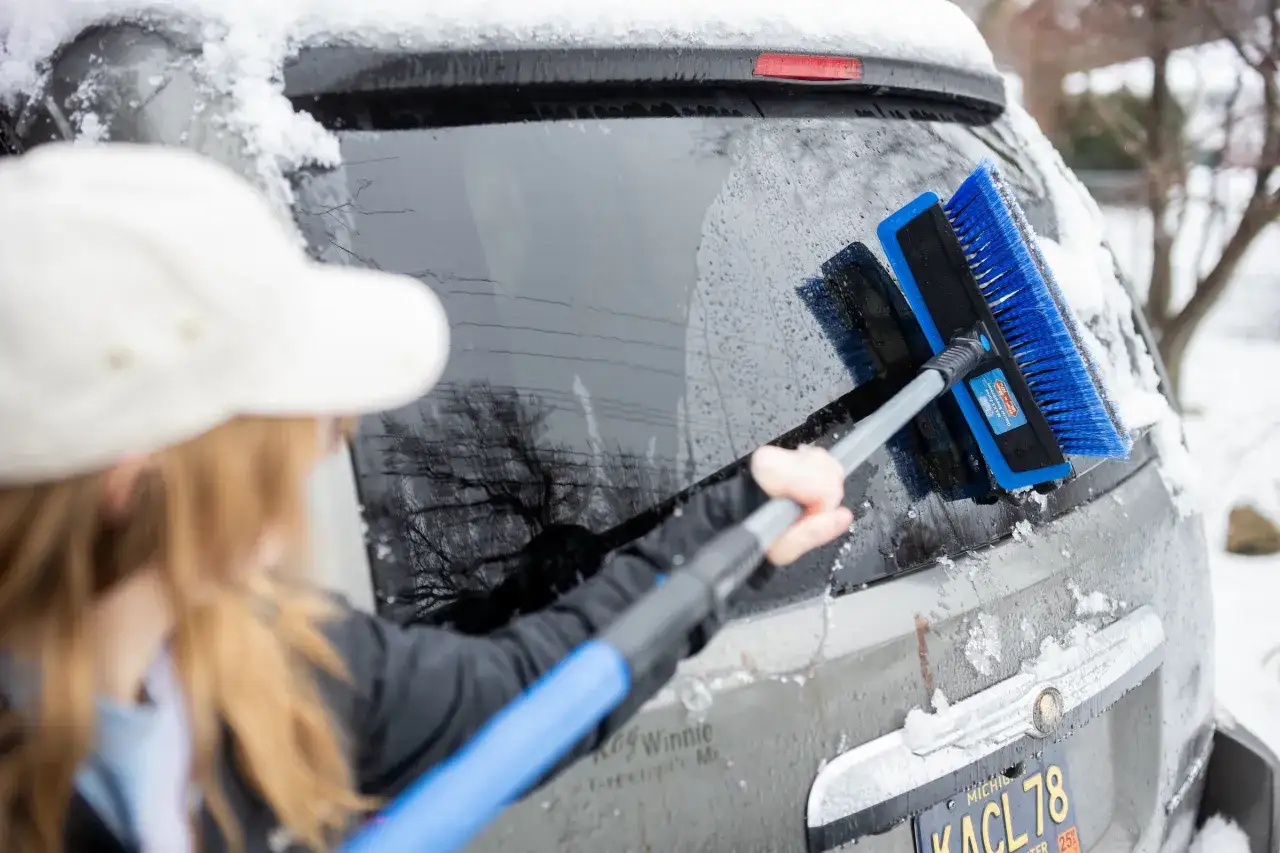 Donna usa una spazzola per neve per sbrinare il vetro della macchina.