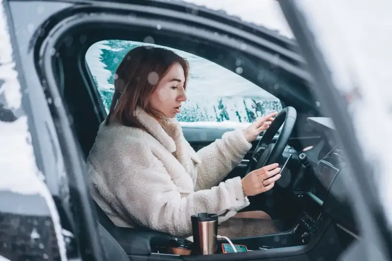 Donna al volante in un'auto coperta di neve, con le mani sul volante. Impara come guidare sulla neve in sicurezza.