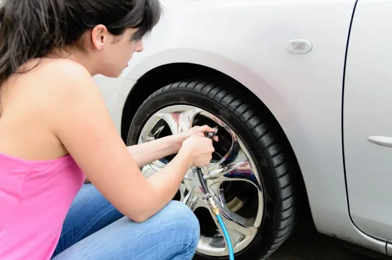 Donna controlla la pressione pneumatici auto, gonfiando la ruota con un compressore.