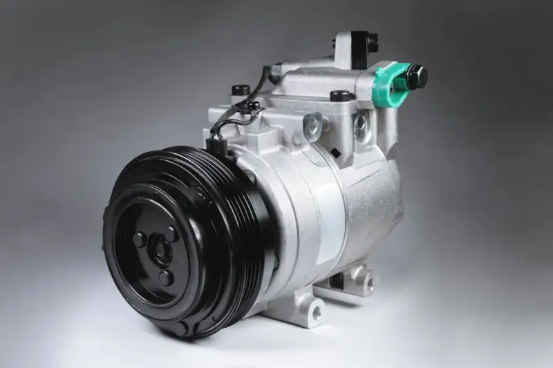 Compressore d'aria condizionata auto: scopri come funziona. Componente metallico argentato con puleggia nera.