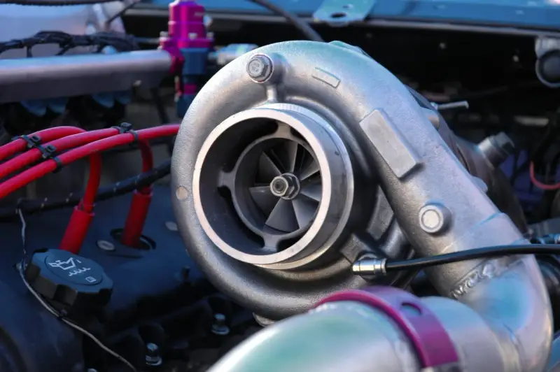 Dettaglio di un motore con un turbo benzina cromato, cavi rossi e un tappo dell'olio.